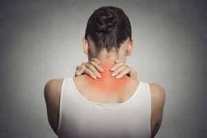 Healthy lifestyle. Back and spine disease. Closeup back view tired female massaging her neck colored in red isolated on gray background